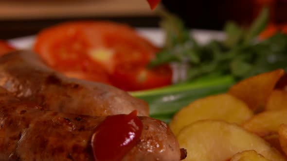 Close-up of the Ketchup Falling on the Fried Sausage on a White Plate