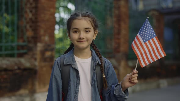 A Little Girl Standing Outside Near School with American Flag