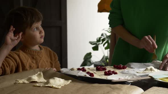 Mother with a son cooking cookies with a cherry at home.