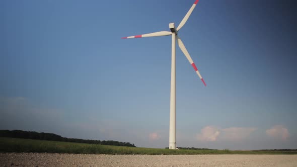 Wide shot of a spinning windmill in the field.