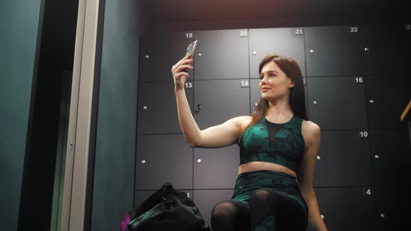 Young Pretty Sportive Woman Taking a Selfie with Her Phone in the Locker Room