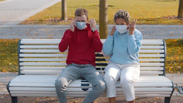 Multiethnic Young Couple Sitting on Bench in Park Putting Off Safety Mask Moving Close and Kissing