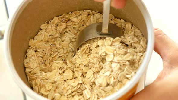 Chef scooping oats into metal measuring cup to make a healthy meal.