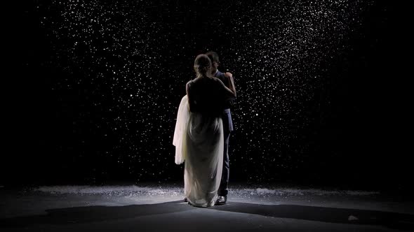 A Charming Couple in Love Dances Against the Background of Falling Snow. A Man in a Suit and a Woman