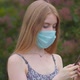 A young girl in a protective medical mask looks at the phone and sends messages - VideoHive Item for Sale