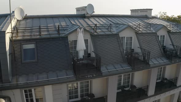 White Wedding Dress Hangs on Special Hanger in Doorway of Balcony of Luxury House Aerial View