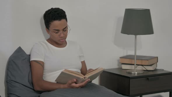 African Woman Reading Book While Sitting in Bed