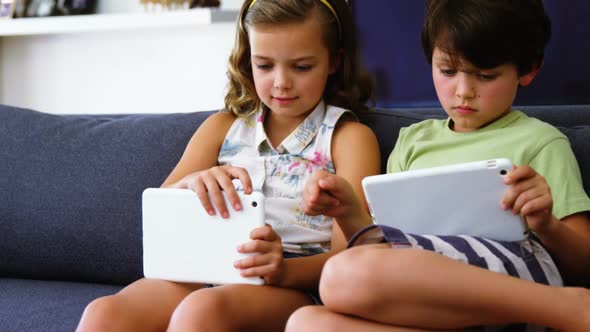 Siblings using digital tablet in living room alt