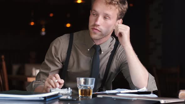 Sad Business Man Sitting at a Table with Whiskey and Reading Papers