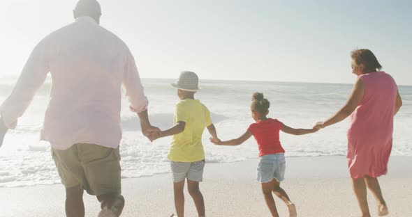 Smiling senior african american couple running with grandchildren on sunny beach