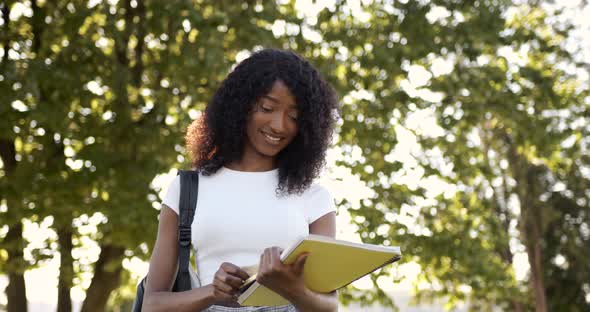 Smiling Black Woman Student Readng Notebook in Park