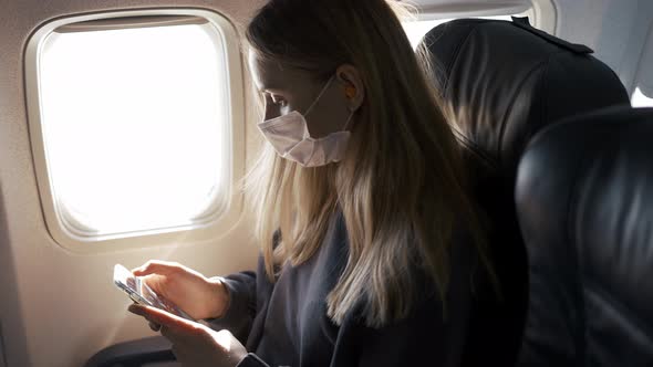 Woman Use a Protection Mask Playing with Her Phone on Airplane