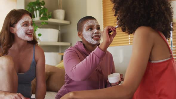 Diverse group of happy female friends trying makeup and talking at home