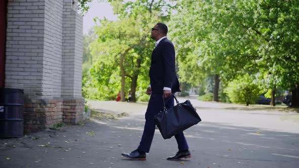 Side View of Confident African American Supervisor with Bag Walking Outdoors and Knocking in Door