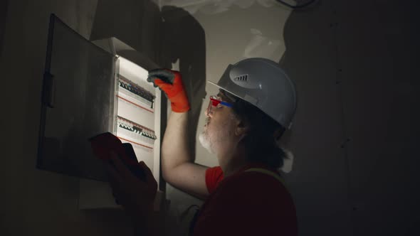 Electrician with Flashlight Switching Fuses in Fuse Box