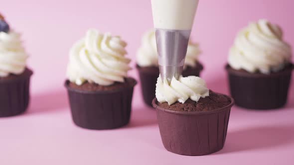 Applying White Cream on a Dark Chocolate Cupcake Cupcake on a Pink Background
