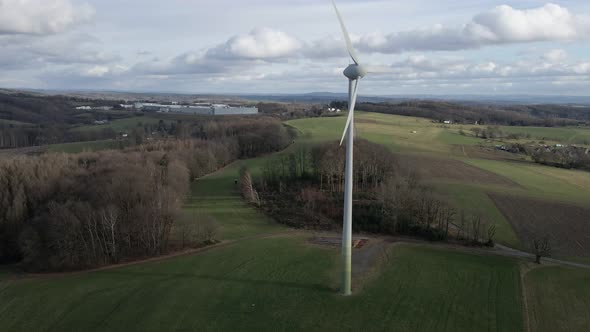 Fast spinning windmill standing in a green field on a cloudy winter day in Germany. Slow aerial pull