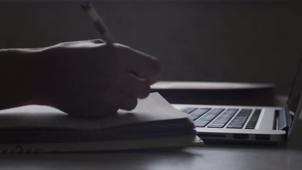 Closeup, hands turn the page, write and make notes in diary. Laptop lays on table. Education concept