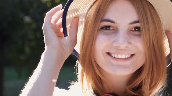 Portrait of pretty positive teenage girl with red hair wearing straw hat and pink earphones 