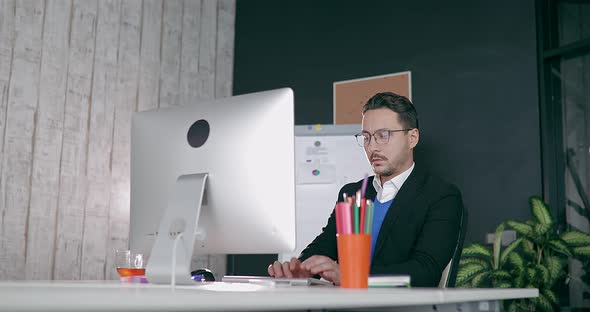 Businessman in Glasses Sits at Computer in Office