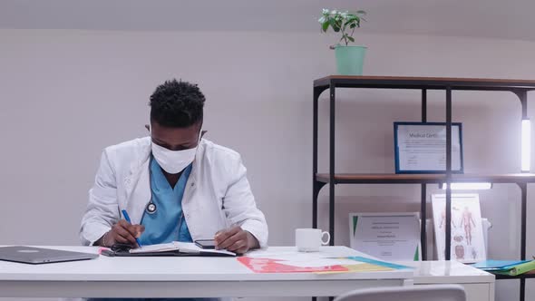 Black Male Doctor Takes Off Face Mask and Hets Happy Sitting at the Desk