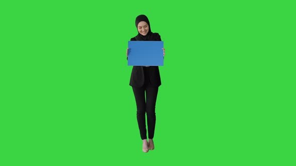 Smiling Arab Woman in Hijab Holding Blank Blue Poster and Looking at Camera on a Green Screen Chroma
