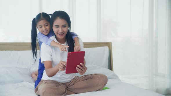 Young asian mom and daughter video call on tablet computer greeting with family together.