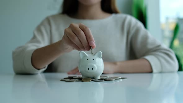 woman putting coin into piggy bank with pile of coins on the table for saving money