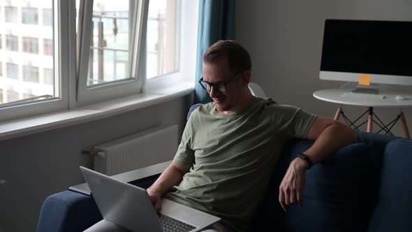 Handsome Young European Man with Beard Sitting on the Sofa with Laptop