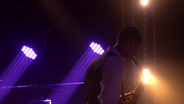 Silhouette a Young Stylish Guy Plays the Golden Shiny Saxophone in the Purple Spotlights on Stage