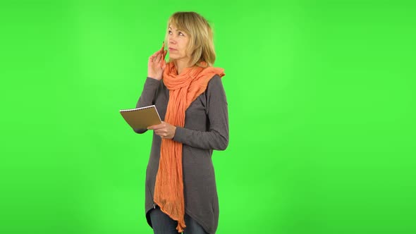 Middle Aged Blonde Woman Is Thinking, Then Writing with Pencil in Notebook