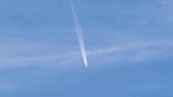 Distant Passenger Jet Plane Flying on High Altitude on Blue Sky with White Clouds Leaving Smoke