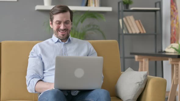 Young Man with Laptop Celebrating Success on Sofa