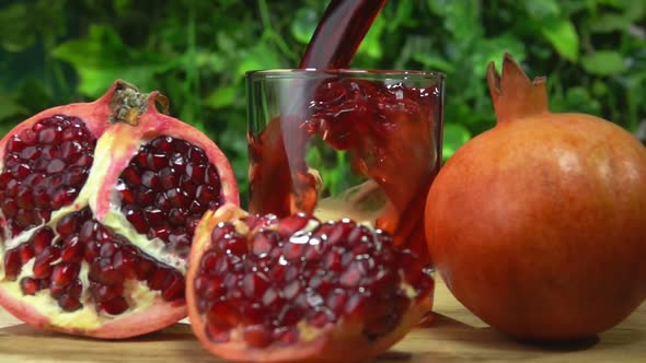 Wave of Red Pomegranate Juice Is Flowing Into Glass Next To the Pomegranates