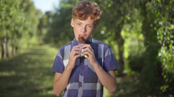 Caucasian Teenage Boy Biting Sweet Chocolate Bar Having Toothache Looking at Camera with Sad Facial