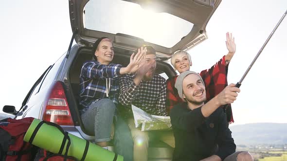 Group of Cheerful Friends Doing Selfie on Smartphone, Sitting Leaning on Trunk of Suv Car