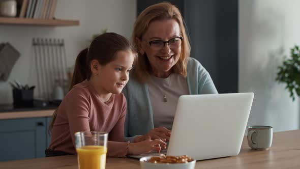 Caucasian grandmother and granddaughter using laptop in the kitchen.