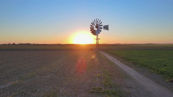 Sunset landscape, cinematic aerial tracking shot capturing old fashioned windpump spinning in the mi