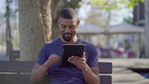 Young Man in Park Searching Information on Tablet, Laughing