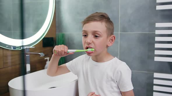 Boy Which Standing Near the Bathroom Mirror and Carefully Cleaning Teeth with Brush alt