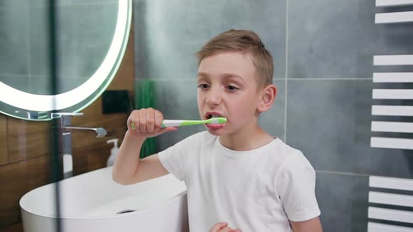Boy Which Standing Near the Bathroom Mirror and Carefully Cleaning Teeth with Brush