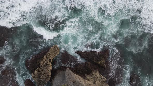 Top down aerial view of giant ocean waves crashing and foaming in coral beach