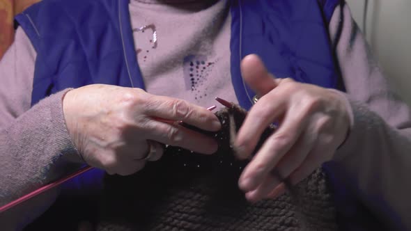 Old adult woman holding needles knitting knitwear scarf relaxing on sofa.