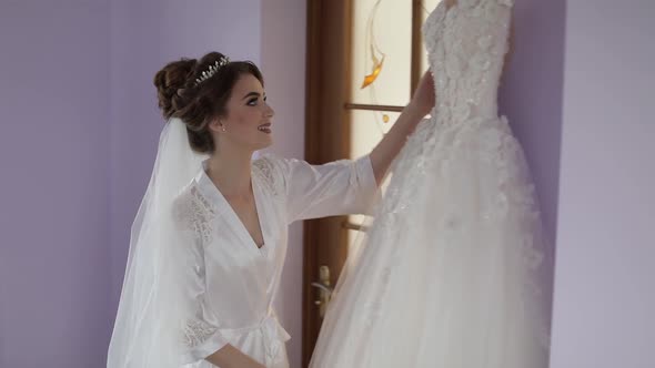 Beautiful and Lovely Bride in Night Gown Stands Near Wedding Dress. Wedding