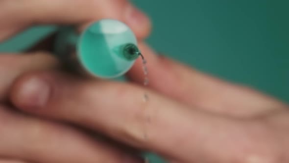 Syringe Needle with Liquid Dripping Drops of Medication in Doctor Hands