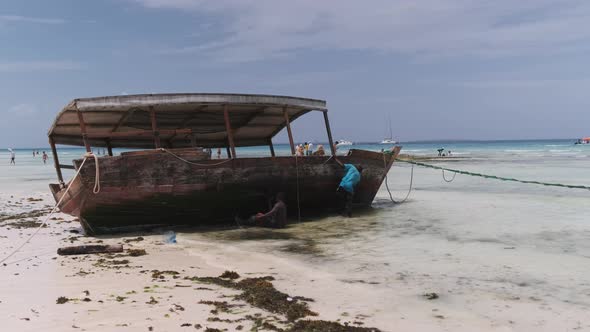 African Fishermen Cleans a Boat From Algae on the Shore at Low Tide Zanzibar