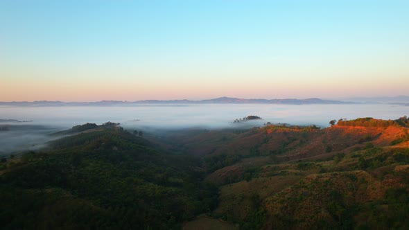 4K aerial view over mountain at sunrise in heavy fog. golden morning sunlight