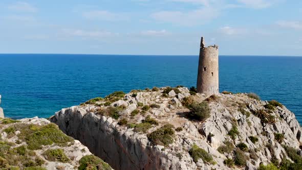 Drone flies over a coastal watchtower, centennial tower on the sea cliff and blue sky with rocks in