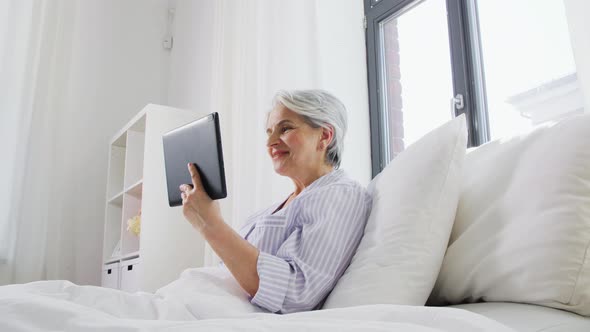 Old Woman with Tablet Pc Having Video Call in Bed