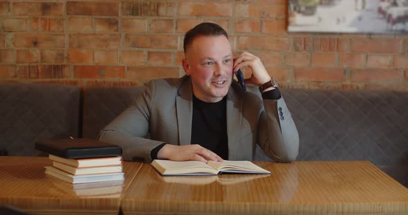 A Man Has A Joyful Conversation On The Phone While Sitting In A Cafe For A Book